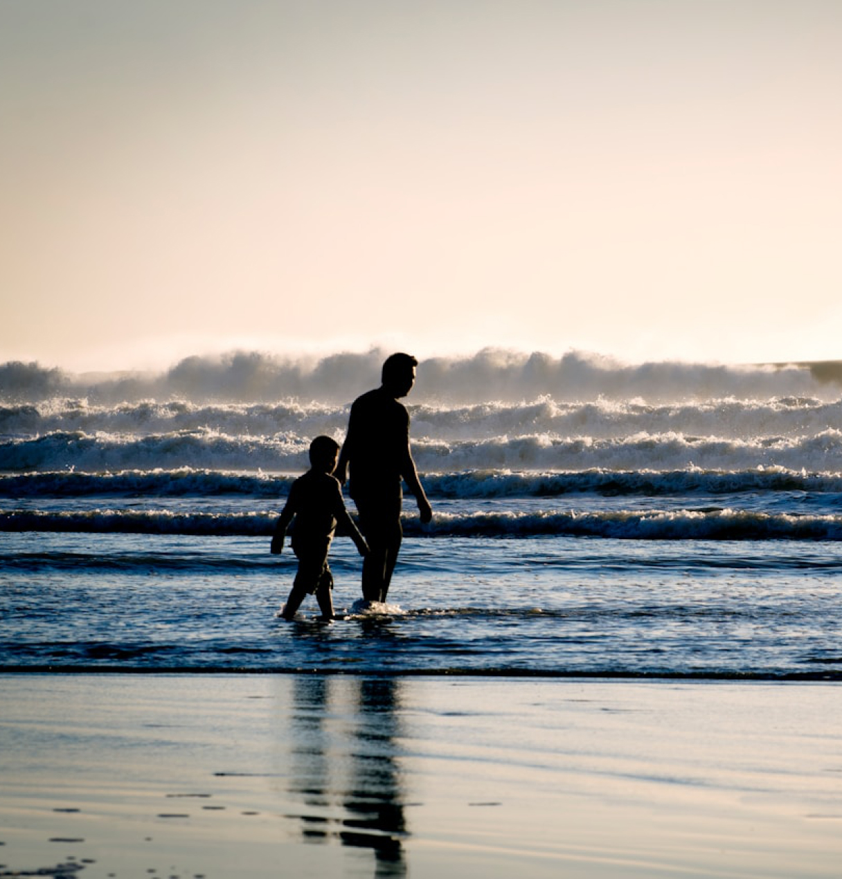 A parent and child walking together on the beach at sunset